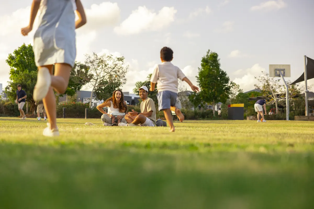 Children running across a park oval while families relax on the grass