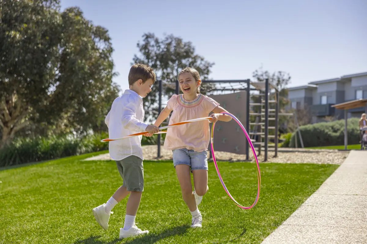 A boy and girl playing with hula hoops on the grass beside a playground at SOUL